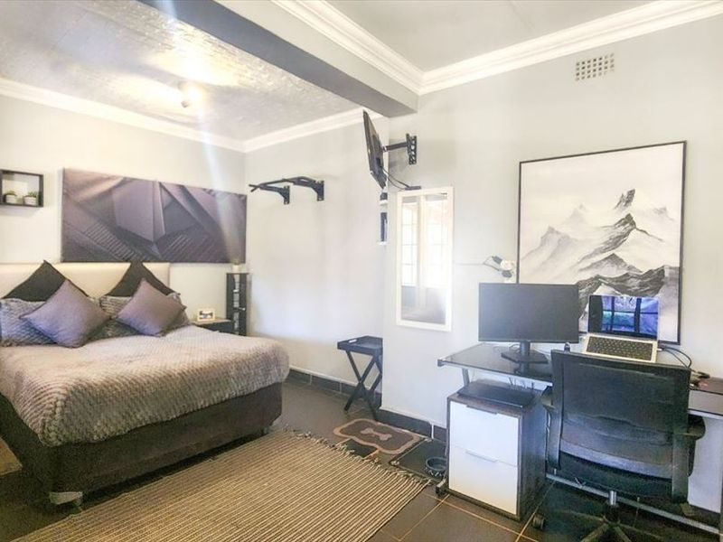 A spacious bedroom featuring tiled flooring, crown molding, and a functional layout suitable for both sleeping and workspace areas.