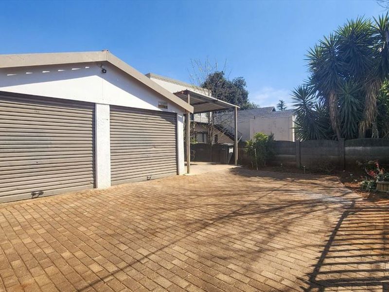 A paved driveway leading to a double garage with roller shutter doors and an adjacent carport, secured by a perimeter wall and metal gate.