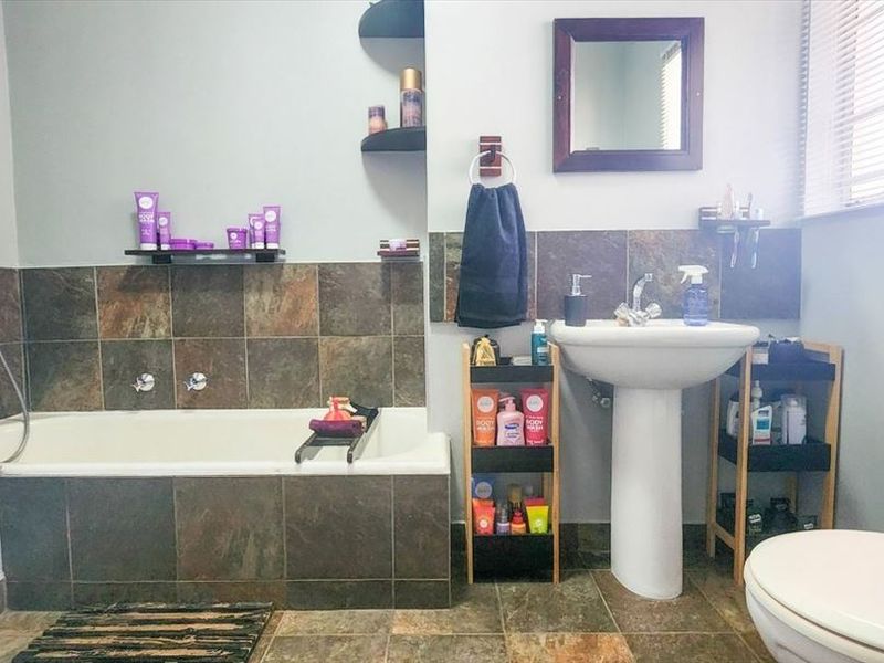A functional bathroom featuring a pedestal basin, built-in bathtub with tiled surround, and tiled flooring, offering a practical layout for daily use.