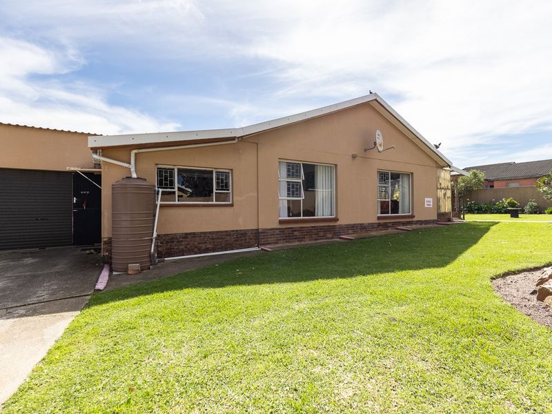 Rear view of the property featuring a single garage, water storage tank, and a well-maintained lawn area.