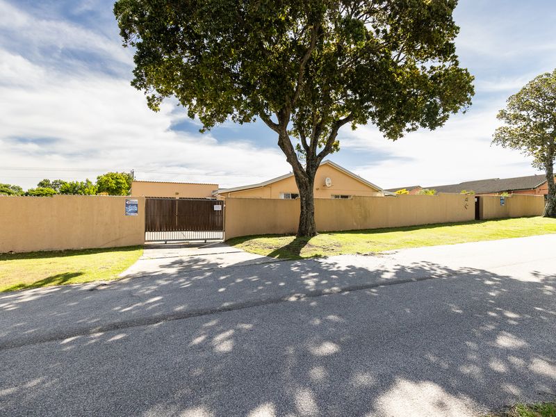 Front view of the property featuring a perimeter wall, gated driveway access, and established trees along the street frontage.
