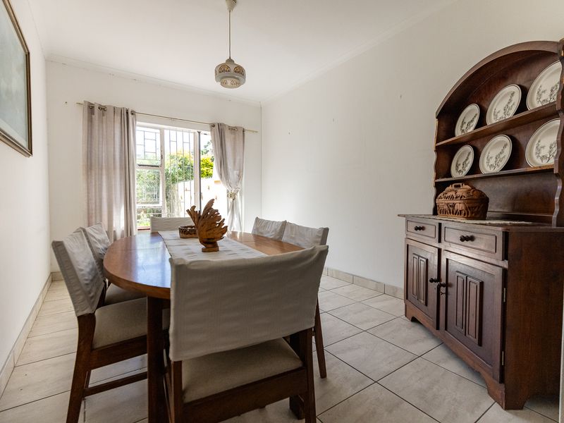 A bright dining room featuring neutral tiled flooring, a central pendant light, and a window fitted with security bars.