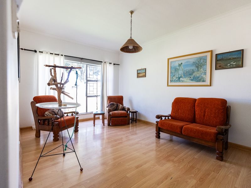 A bright living room featuring laminate flooring, a pendant light fixture, and large windows fitted with security bars.