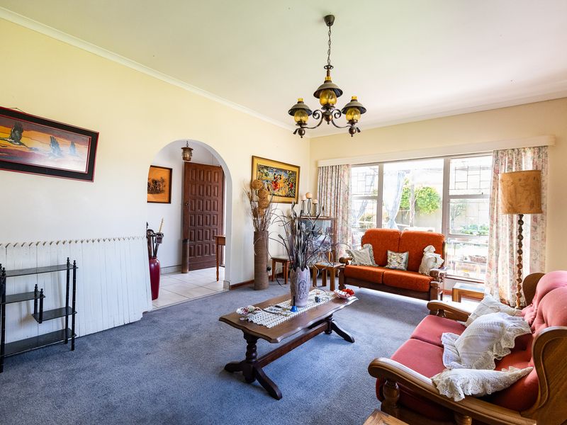 A spacious living room featuring an arched entryway, large windows providing natural light, and classic coving details, offering a comfortable and traditional living space.