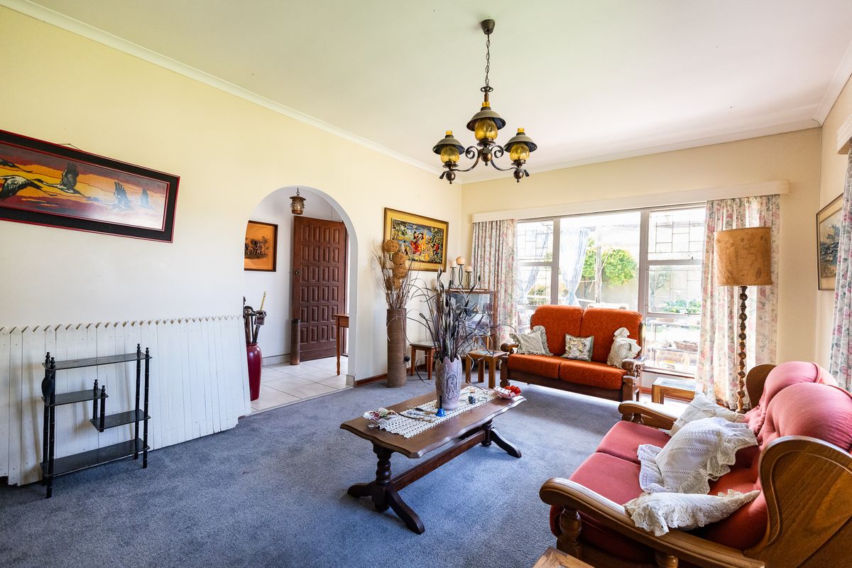 A spacious living room featuring an arched entryway, large windows providing natural light, and classic coving details, offering a comfortable and traditional living space.