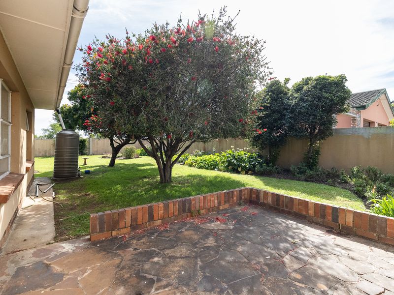 A rear garden area featuring a stone paved patio with a low brick retaining wall, established trees, and a rainwater tank.