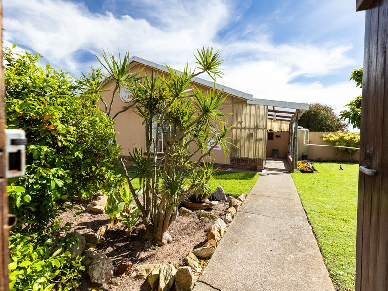 A view of the rear garden featuring a concrete walkway leading to a covered patio area and a water tank.