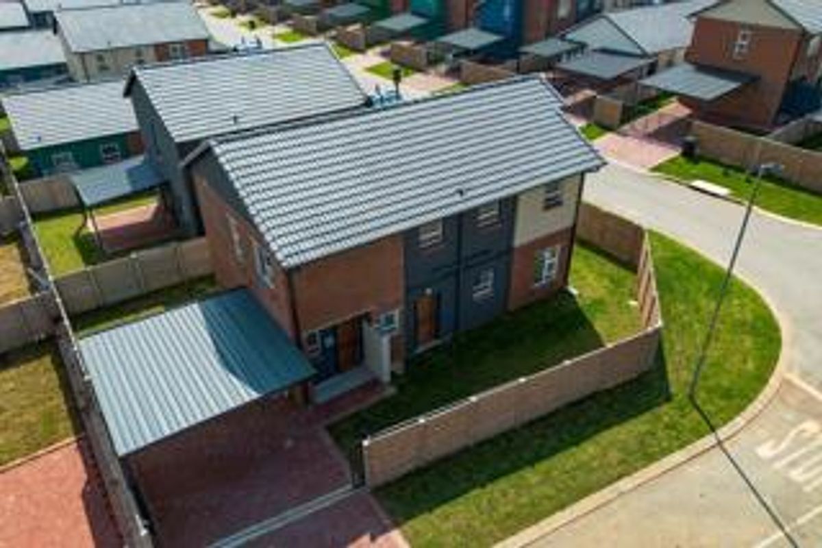Aerial view of a modern two-story residential house featuring a tiled roof, brick exterior, private carport, and a fenced garden area.