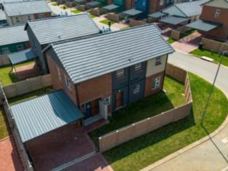 Aerial view of a modern two-story residential house featuring a tiled roof, brick exterior, private carport, and a fenced garden area.