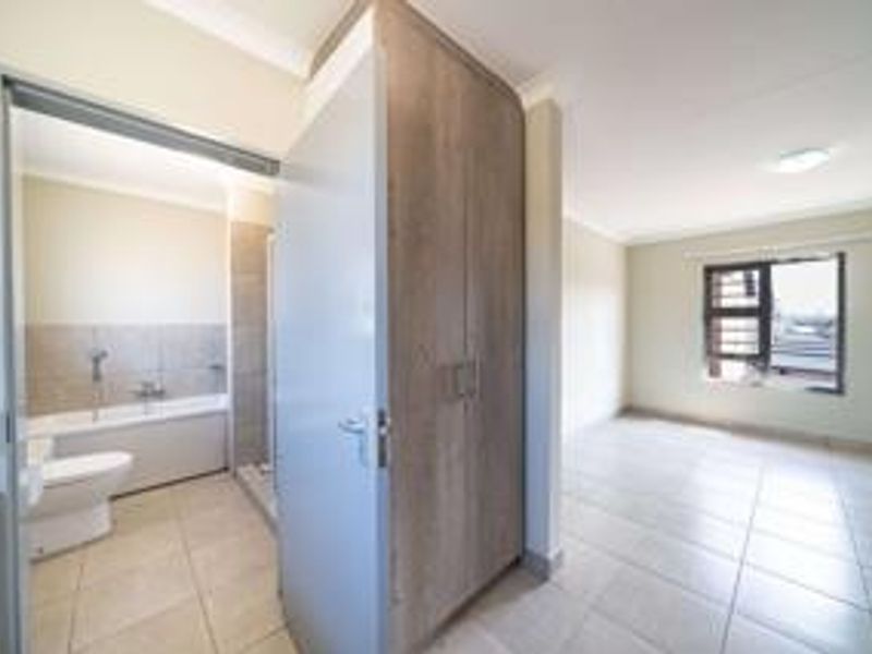 A spacious, empty bedroom featuring tiled flooring, a built-in wardrobe, and an attached en-suite bathroom with a bathtub and toilet.