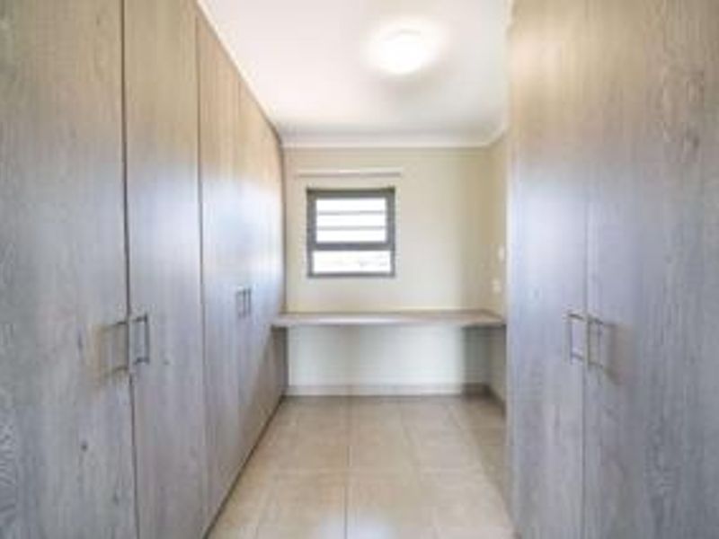 A clean, empty bedroom featuring extensive built-in cabinetry and a dedicated built-in desk area with tiled flooring.
