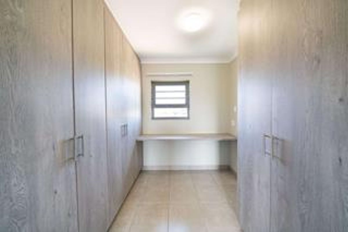 A clean, empty bedroom featuring extensive built-in cabinetry and a dedicated built-in desk area with tiled flooring.