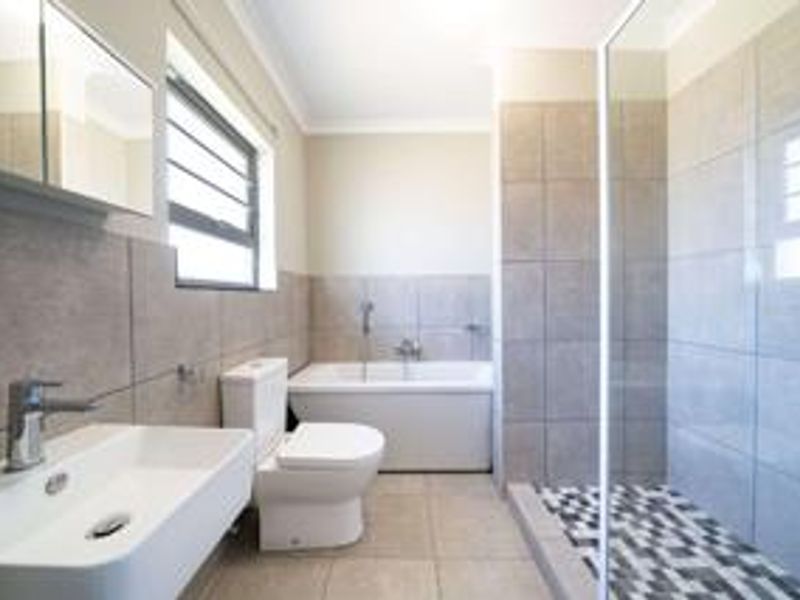 Modern bathroom featuring a wall-mounted vanity, back-to-wall toilet, built-in bathtub, and a separate shower enclosure with mosaic floor tiling.
