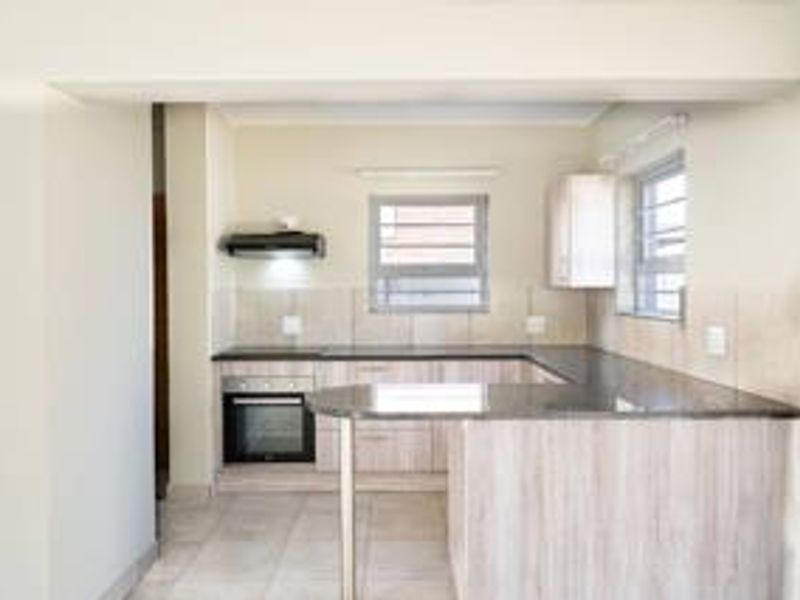 A clean, modern kitchen featuring light wood-finish cabinetry, dark granite countertops, a built-in oven, and an extractor fan with neutral tiled finishes.