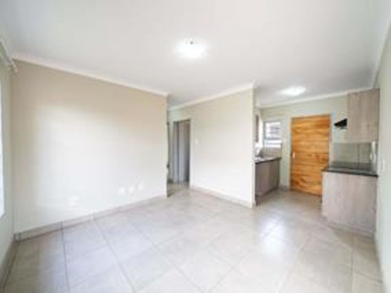 An open-plan living and kitchen area featuring neutral tiled flooring, built-in cabinetry, and a solid wood door, offering a clean and versatile living space.