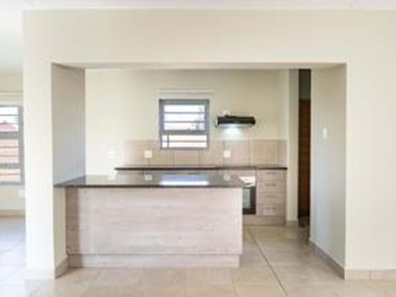 A clean, modern kitchen featuring granite countertops, built-in cabinetry, an integrated oven, and an extractor fan, finished with neutral tiled flooring.