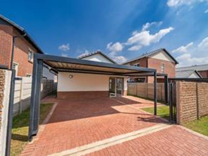 A well-maintained front exterior featuring a brick-paved driveway, a modern carport structure, and secure boundary walls.