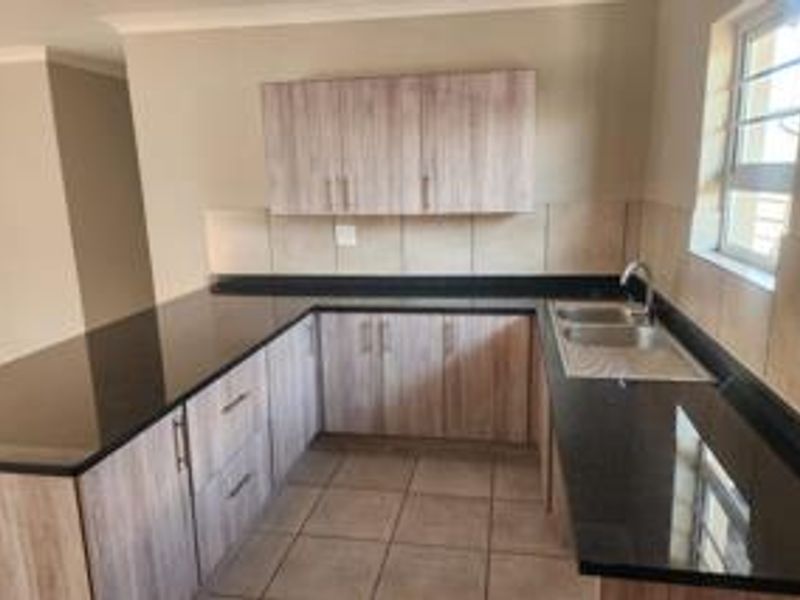A clean and functional kitchen featuring modern laminate cabinetry, dark granite countertops, and a double bowl stainless steel sink with tiled splashbacks.