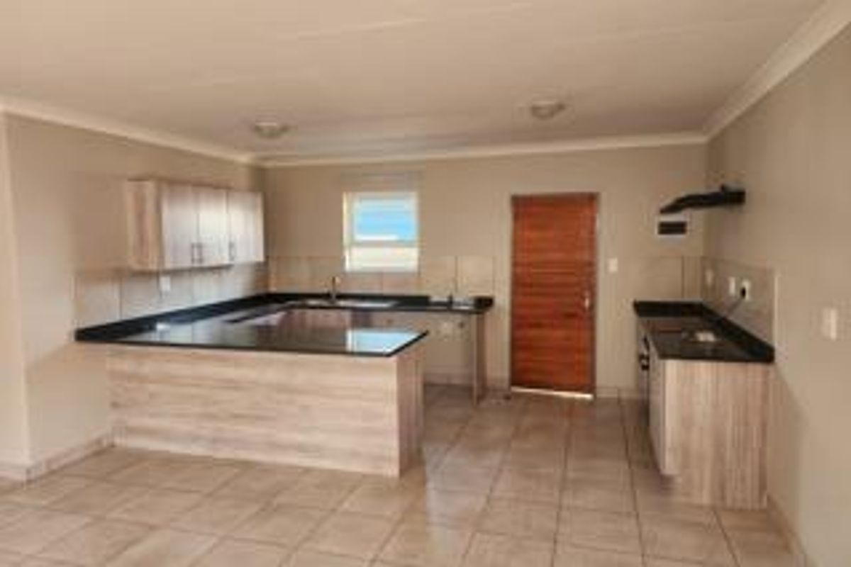 A spacious, empty kitchen featuring light wood-look cabinetry, dark granite countertops, tiled flooring, and a functional layout with an integrated extractor fan.
