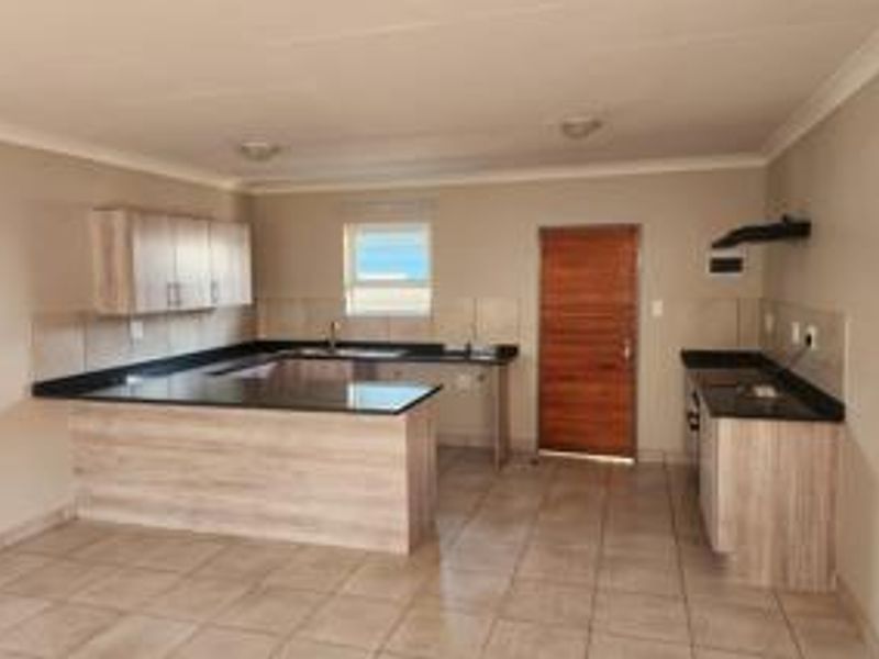 A spacious, empty kitchen featuring light wood-look cabinetry, dark granite countertops, tiled flooring, and a functional layout with an integrated extractor fan.