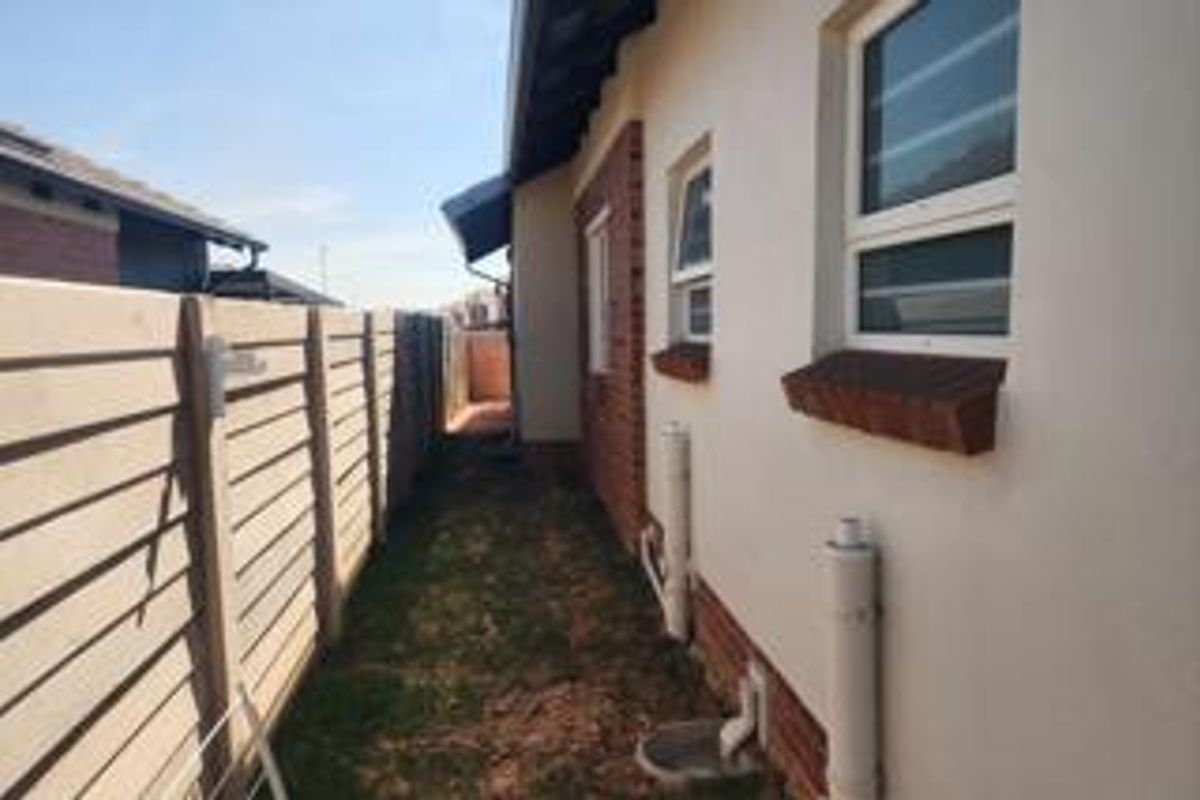 A side passage of the house featuring a precast concrete boundary wall, plastered exterior walls with brick accents, and functional drainage infrastructure.