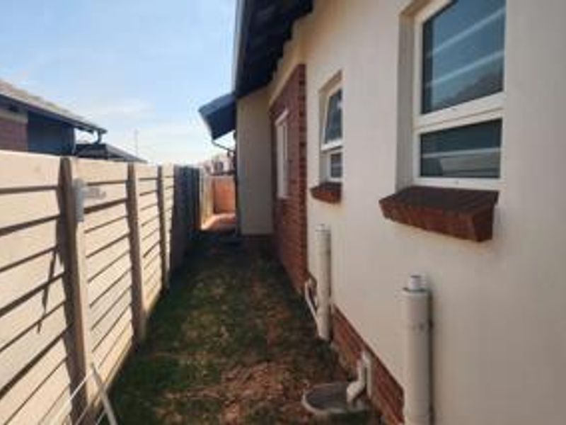A side passage of the house featuring a precast concrete boundary wall, plastered exterior walls with brick accents, and functional drainage infrastructure.