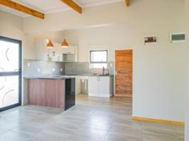 An open-plan living and kitchen area featuring exposed timber ceiling beams, modern cabinetry, a kitchen island, and neutral tiled flooring throughout.