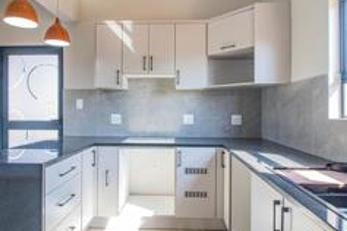 A modern, clean kitchen featuring light-toned cabinetry, dark stone countertops, a tiled backsplash, and contemporary pendant lighting in an open, bright space.
