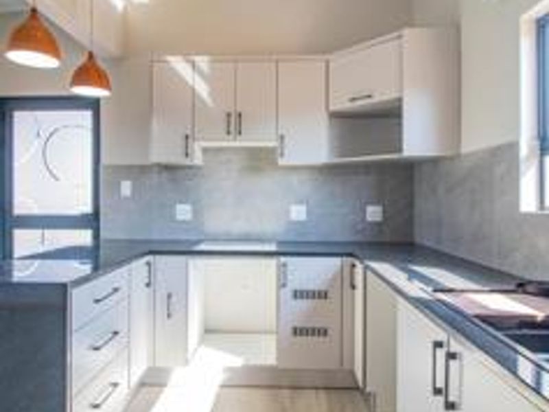A modern, clean kitchen featuring light-toned cabinetry, dark stone countertops, a tiled backsplash, and contemporary pendant lighting in an open, bright space.