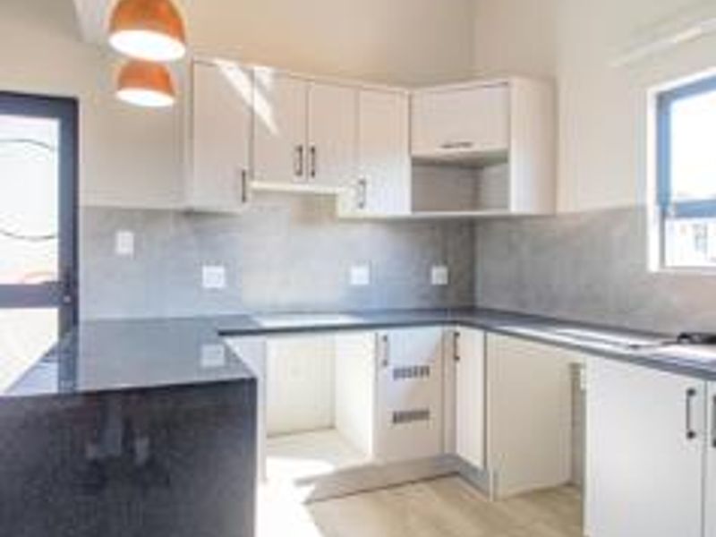 A clean, modern kitchen featuring white cabinetry, dark stone countertops, a tiled backsplash, and integrated sink, presented in a bright, empty space.