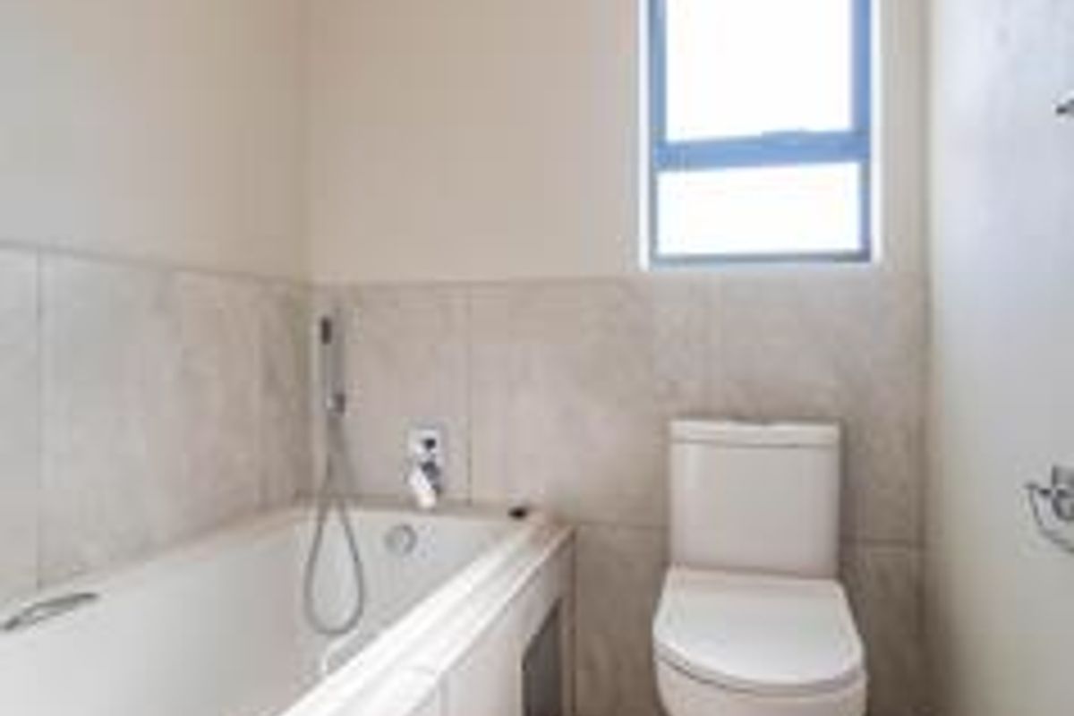 A clean, functional bathroom featuring a built-in bathtub, modern toilet, and neutral wall tiling with natural light from a window.
