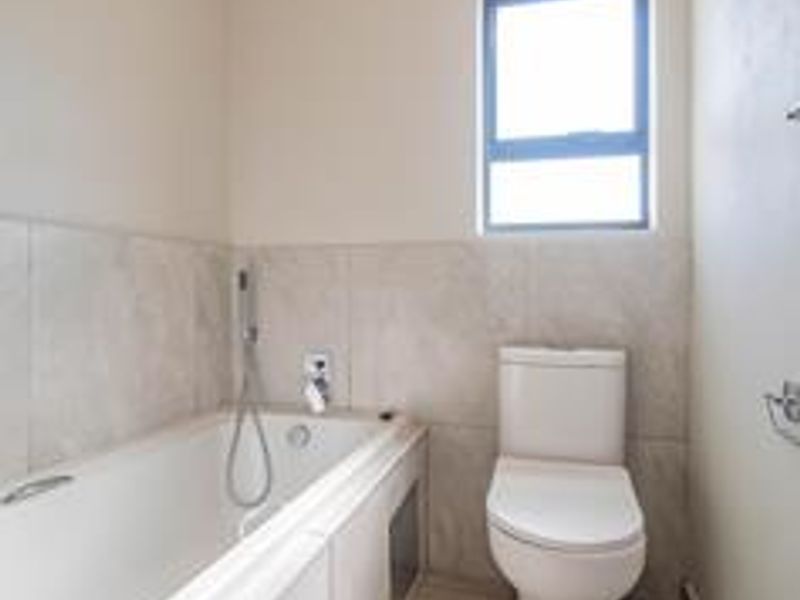 A clean, functional bathroom featuring a built-in bathtub, modern toilet, and neutral wall tiling with natural light from a window.