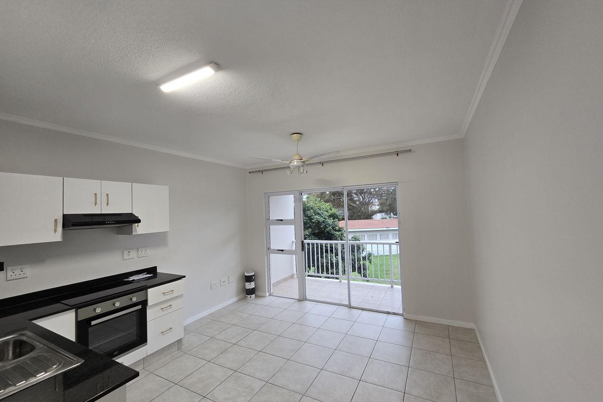 Open-plan kitchen and living area featuring tiled floors, built-in cabinetry with granite countertops, and direct access to a private balcony.
