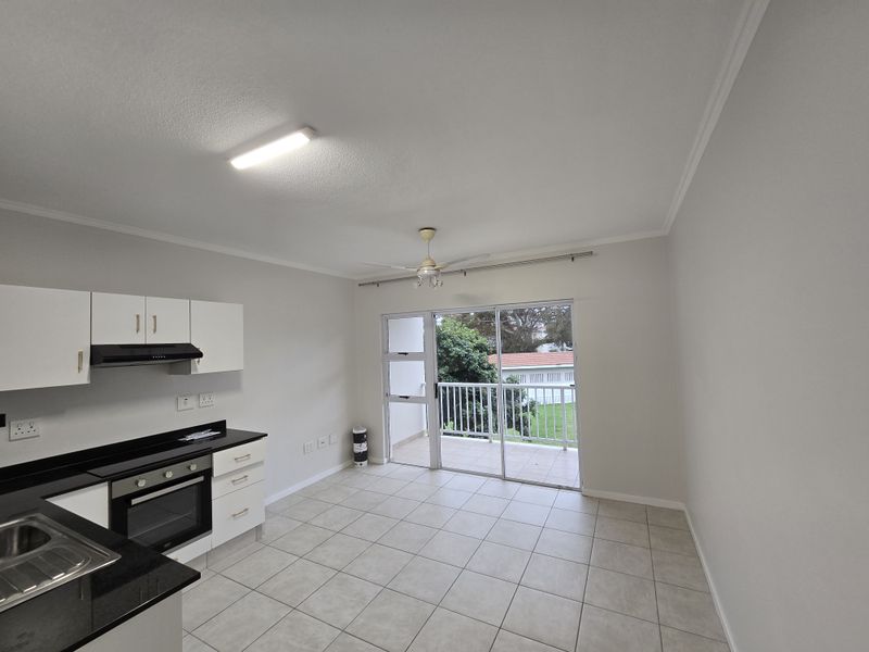 Open-plan kitchen and living area featuring tiled floors, built-in cabinetry with granite countertops, and direct access to a private balcony.
