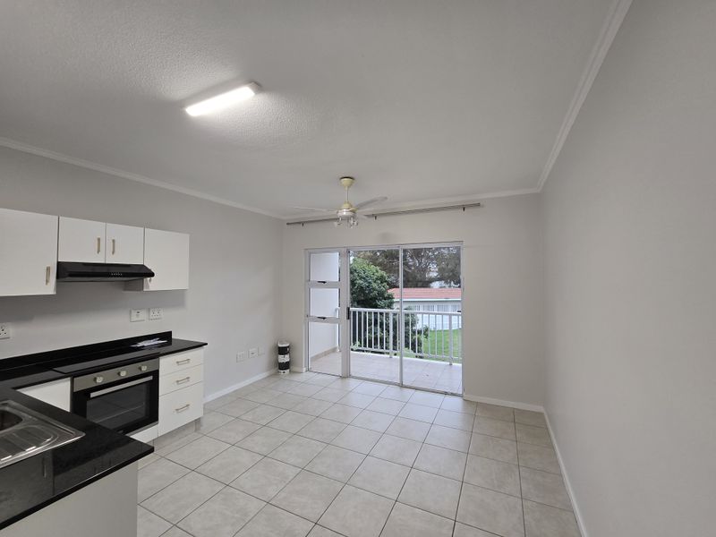 Open-plan kitchen and living area featuring tiled floors, modern cabinetry, built-in appliances, and direct access to a private balcony.