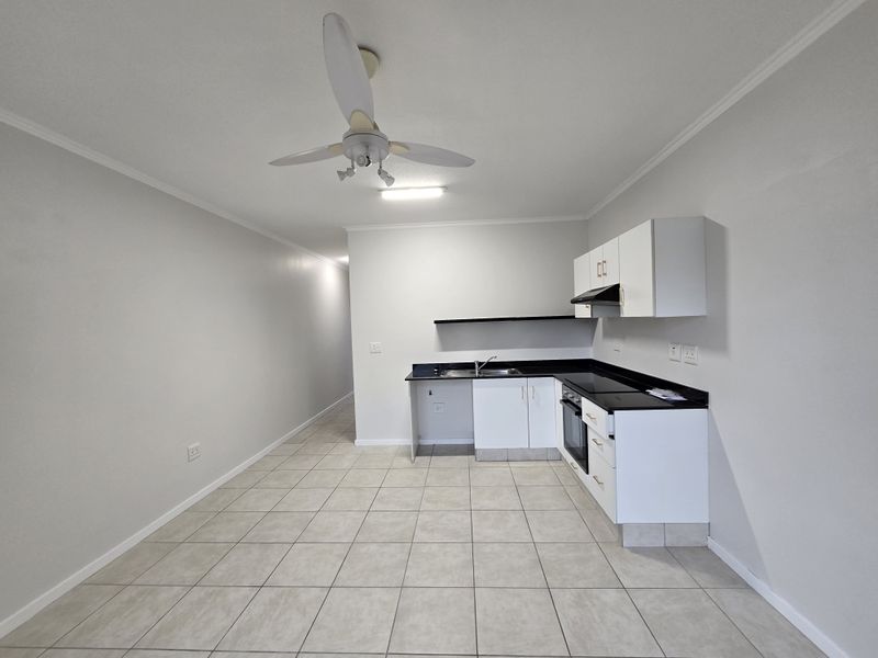 An open-plan kitchen area featuring white cabinetry, black countertops, built-in oven, extractor fan, and neutral ceramic floor tiles.