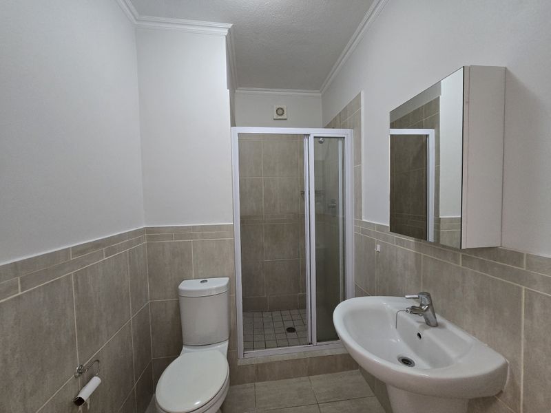 A clean and functional bathroom featuring a shower enclosure, pedestal basin, and wall-mounted medicine cabinet with neutral tiled finishes.