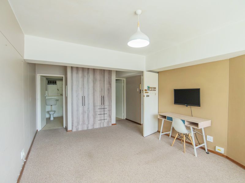 A bedroom featuring built-in wardrobes, neutral carpeting, and an en-suite bathroom access, offering a functional and well-lit living space.