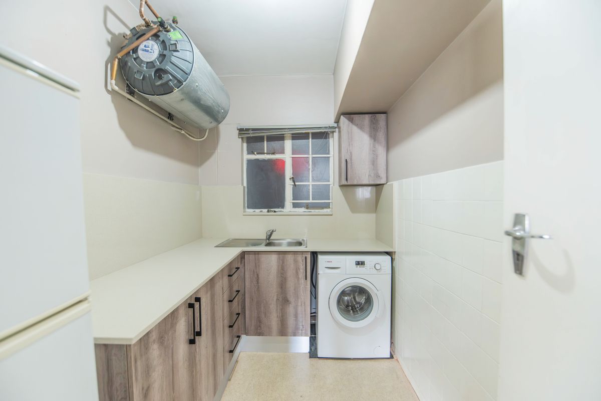 Functional laundry area featuring built-in cabinetry, laminate countertops, a stainless steel sink, and a wall-mounted geyser with tiled splashbacks.