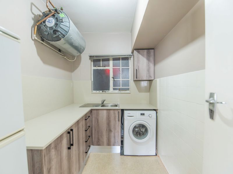 Functional laundry area featuring built-in cabinetry, laminate countertops, a stainless steel sink, and a wall-mounted geyser with tiled splashbacks.