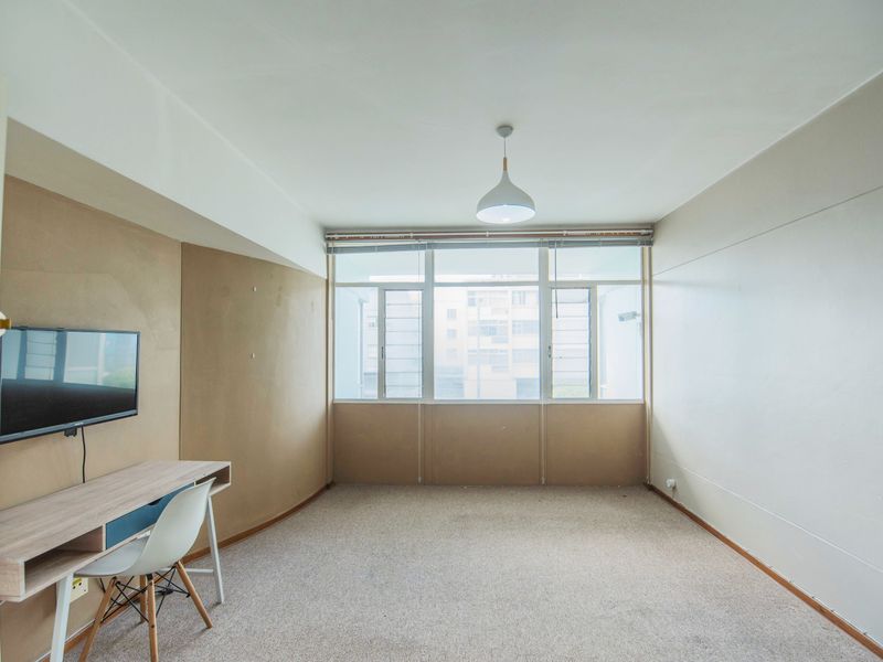 A spacious, carpeted bedroom featuring a large window that provides natural light and a central pendant light fixture.