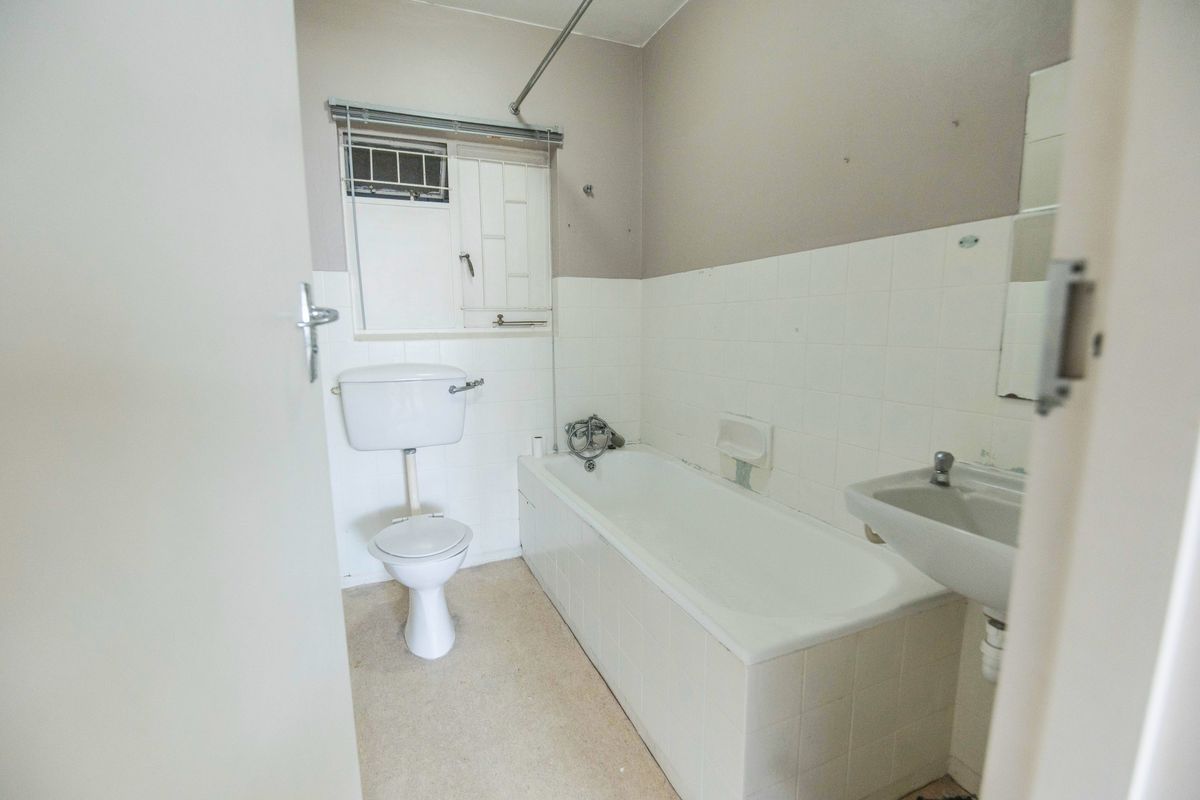 A functional bathroom featuring a standard bathtub, toilet, and wall-mounted basin with tiled splashbacks, offering a blank canvas for renovation.