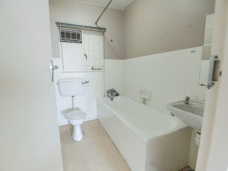 A functional bathroom featuring a standard bathtub, toilet, and wall-mounted basin with tiled splashbacks, offering a blank canvas for renovation.