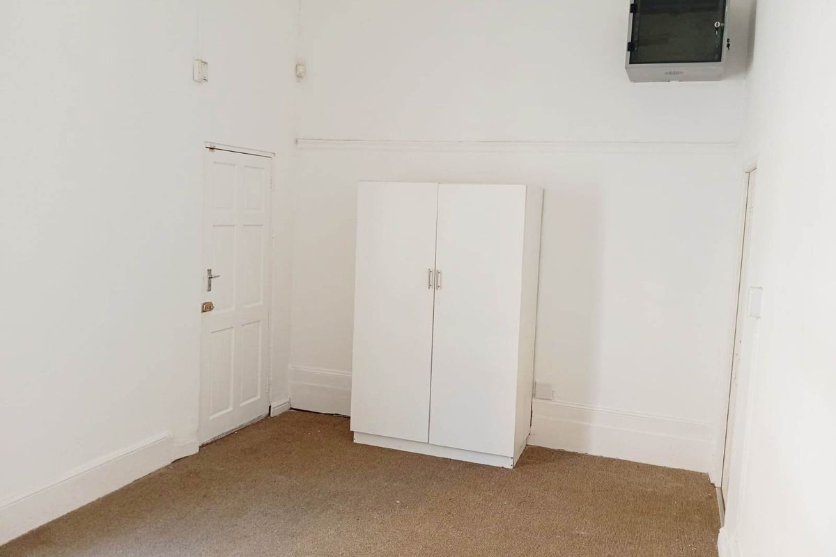 A simple, empty bedroom featuring white walls, a built-in wardrobe, and carpeted flooring.