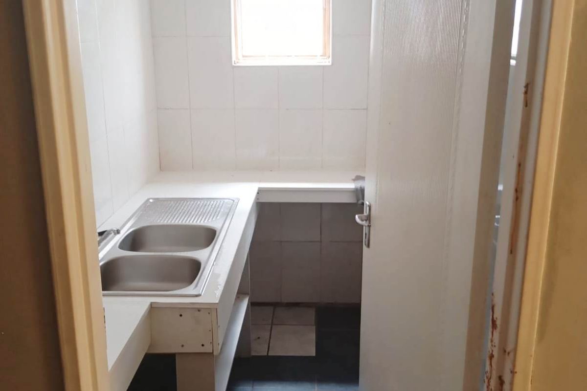 A functional laundry area featuring a double stainless steel sink, tiled splashbacks, and tiled flooring, ready for modernization.