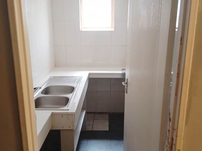 A functional laundry area featuring a double stainless steel sink, tiled splashbacks, and tiled flooring, ready for modernization.