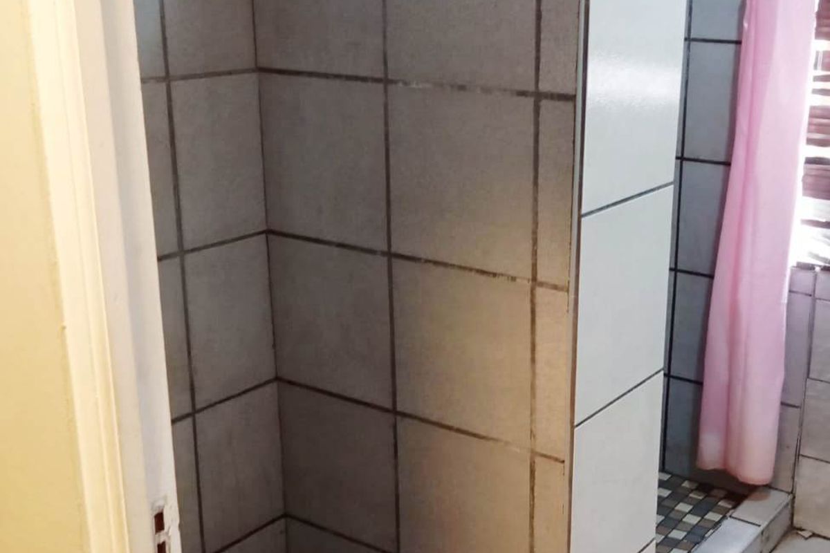 A functional bathroom featuring a tiled shower enclosure with a raised threshold and tiled flooring.