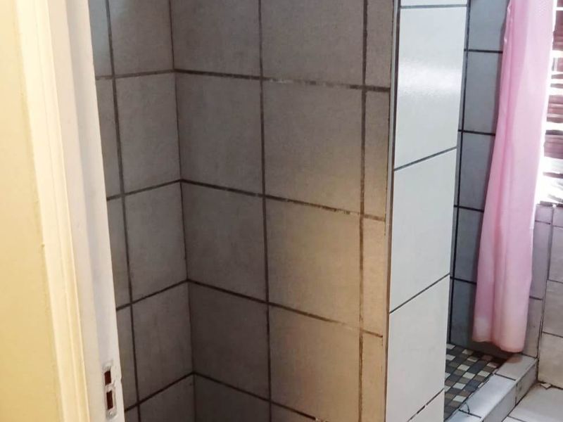 A functional bathroom featuring a tiled shower enclosure with a raised threshold and tiled flooring.