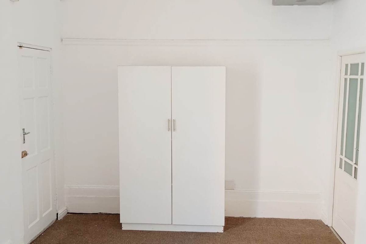 An empty bedroom featuring a built-in wardrobe, carpeted flooring, and classic panelled doors, offering a blank canvas for potential renovation or styling.