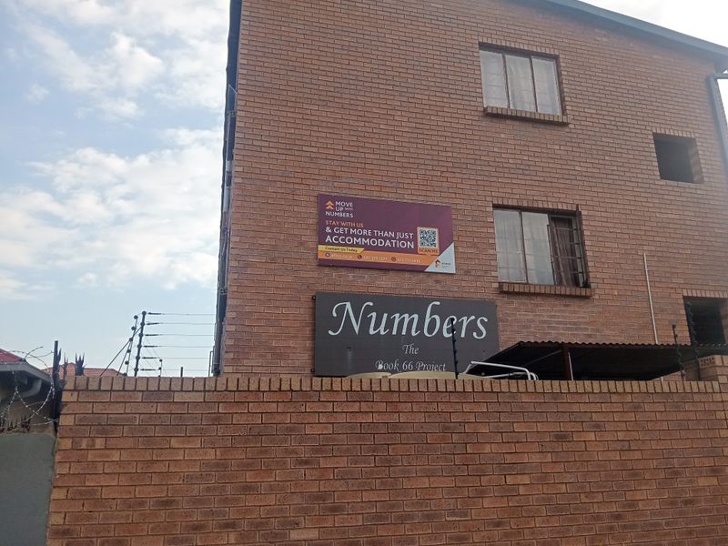 Exterior view of a multi-story face brick apartment building featuring security fencing and prominent signage.